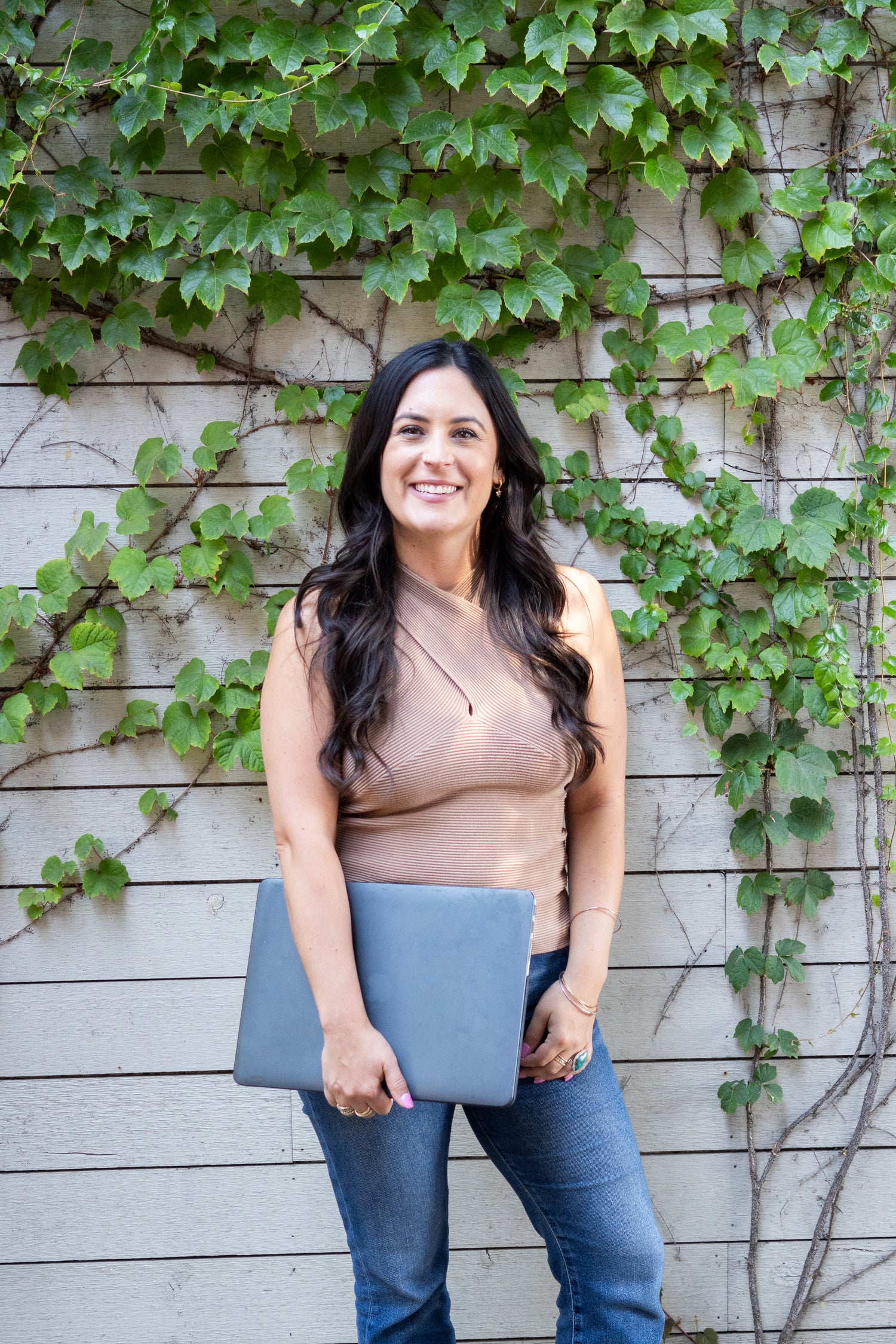 Woman holding a black laptop against a wall with green ivy